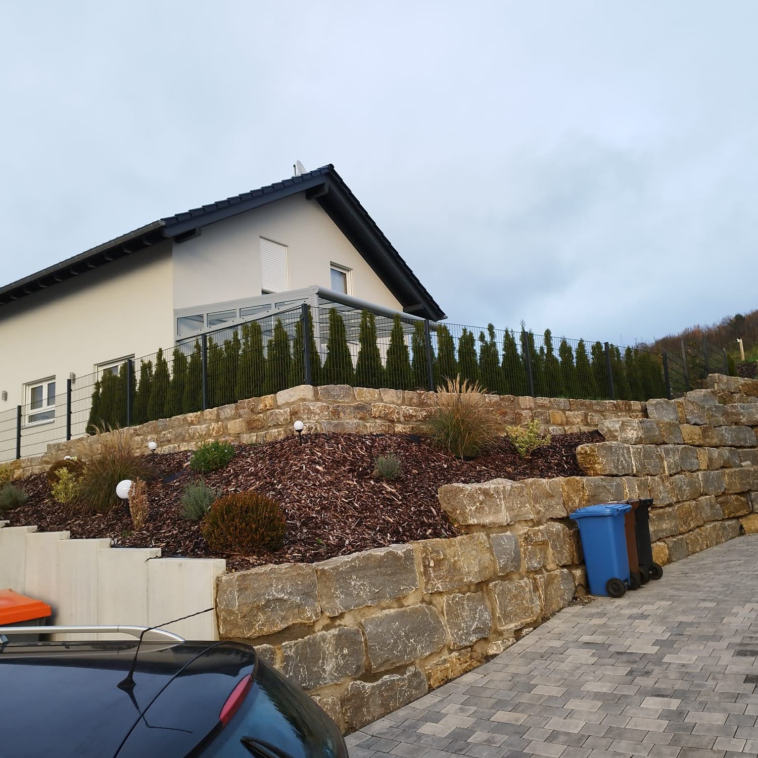 Fertige Hanggestaltung mit Natursteinmauer, Bepflanzung und Pflasterfläche